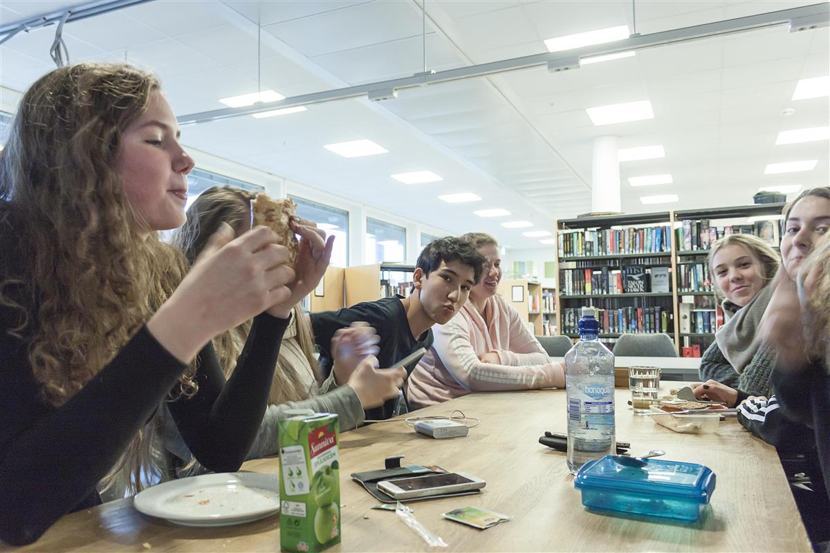 Foto. Elever sitter rundt et bord og spiser lunsj - Klikk for stort bilde
